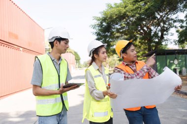 Aralarında bir mühendis, bir proje yöneticisi ve bir işçinin de bulunduğu üç inşaat işçisi, planları analiz ediyor ve aktif bir şantiyede planları tartışıyorlar..