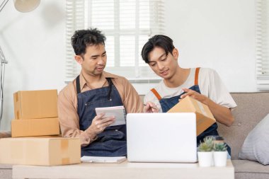 Yaratıcı bir LGBT çifti çevrimiçi işlerine odaklanmış ürünleri tartışıyor ve rahat bir ofis ortamında eşyalar paketliyor..