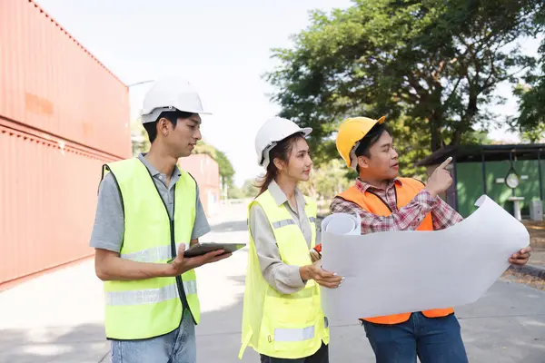 Aralarında bir mühendis, bir proje yöneticisi ve bir işçinin de bulunduğu üç inşaat işçisi, planları analiz ediyor ve aktif bir şantiyede planları tartışıyorlar..
