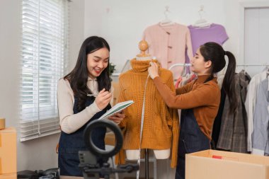İki farklı perakende işçisi not almak ve bir mankenin üzerindeki süveteri ayarlamak için çalışırken aynı zamanda modaya uygun bir perakende satış ayarında envanter düzenliyor..