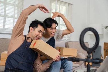 İki canlı sosyal medya pazarlamacısı neşeli jestler yapıyor ve sıcak ofislerinde canlı bir canlı yayın sırasında ürünlerini sergiliyorlar. Neşeli bir atmosfer yaratıyorlar..