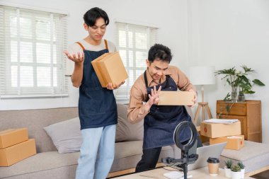 İki dinamik sosyal medya pazarlamacısı sıcak bir ev ofisinde canlı yayın sırasında çevrimiçi seyircilerine ürün paketleri sunuyor ve sergiliyor..