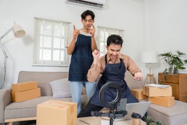 Canlı bir canlı yayın sırasında canlı iki sosyal medya pazarlamacısı dans ediyor ve çevrimiçi seyircileriyle meşgul oluyor, şık ev ofislerinde ürün paketleriyle çevrili..