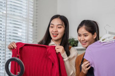 İki kadın coşkuyla giysi sunuyor, keyif paylaşıyor ve şık ev ofislerinde online satışlara hazırlanıyor..