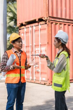 Bir inşaat mühendisi, nakliye konteynırlarının yanında proje özellikleri ve iletişim telsiziyle ilgili ayrıntılı bir konuşma yapar..