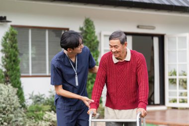 Dost canlısı bir sağlık uzmanı, yürüteç kullanan yaşlı bir adamı destekliyor. Açık havada neşe ve bağımsızlığı teşvik ediyor..