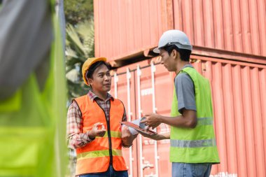 İki inşaat mühendisi, nakliye konteynırları yakınlarında lojistik ve proje planlaması, sergilenen takım çalışması ve sorun çözme konularında ayrıntılı bir tartışmaya giriştiler..