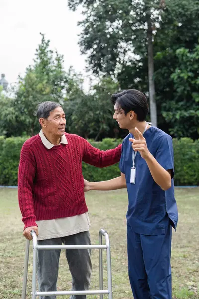 Şefkatli genç bir bakıcı yaşlı bir adamla yürüteç kullanarak ilişki kurar, yemyeşil bir bahçe ortamında anlamlı bir konuşma yapar, bağlantıyı güçlendirir ve duygusal destek sağlar..