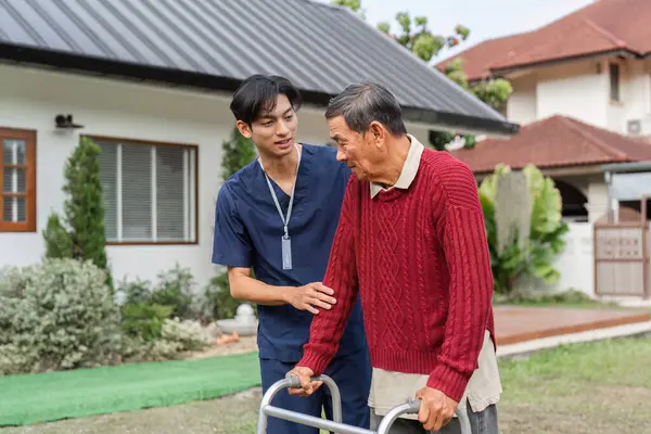 Kendini adamış bir sağlık uzmanı yaşlı bir adama yürüyüşçüsü ile nazikçe yardım eder, dışarıda huzurlu bir ortamda duygusal bağlar ve destek sağlar..