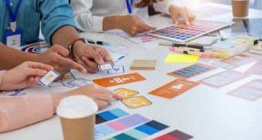 UI UX prototiplerini ve kullanıcı deneyimini geliştirmek için renk şemalarını tartışan yaratıcı bir tasarım oturumuna katılan çeşitli bir ekip.