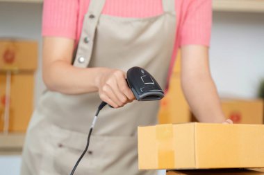 Bir kadın, küçük işletmesindeki bir paketi işlemek için barkod tarayıcısı kullanıyor. Nakliyattaki lojistik ve verimliliği vurguluyor..