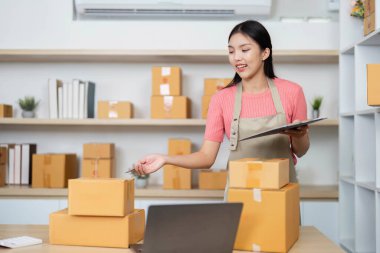 Genç bir girişimci paketleri verimli bir şekilde organize ediyor ve küçük iş yerinde notlar alıyor, kendini işine adamış ve üretkenliğini gösteriyor..