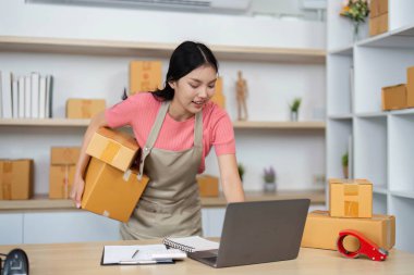 Bir proaktif girişimci, küçük işletme lojistiğini örnek göstererek, dizüstü bilgisayarıyla koordine ederken paketleri kaldırır.