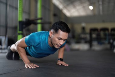 İyi donanımlı bir spor salonunda şınav çeken odaklanmış bir adam, fitness ve güç eğitimini vurguluyor..