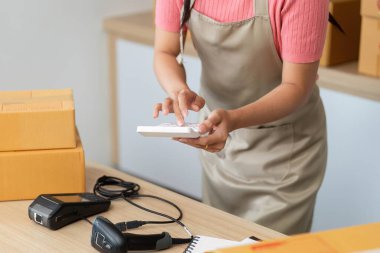 Bir kadın, küçük işletmesindeki nakliye işlerini yönetirken mobil bir cihazla etkileşime giriyor ve lojistikteki modern teknolojiyi sergiliyor..