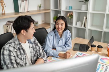 İki UX ve UI tasarımcısı parlak bir ofiste tasarım elemanları ve renk paletleri hakkında yaratıcı bir tartışmaya giriştiler..