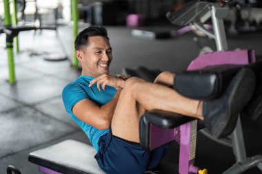 Spor makinesinde bacak egzersizi yapan bir adam spor salonuna ve sağlıklı yaşama karşı olumlu bir tavır sergiliyor..