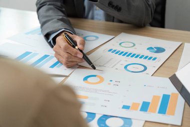 Odaklanmış bir işadamı, kurumsal bir ortamda anahtar kavrayışları vurgulayarak finansal tablolar ve verileri tartışır..