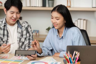 Genç bir erkek ve kadın ortak bir UX ve UI tasarım oturumuna katılıyor, bir tablo üzerinde renk seçenekleri ve düzen tasarımlarını keşfediyor.