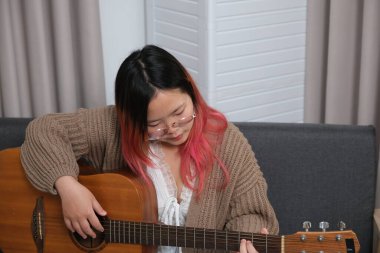 Kızıl saçlı bir kadın gitar çalıyor. O, gözlük ve kahverengi bir kazak giyiyor. Gitar kanepede.