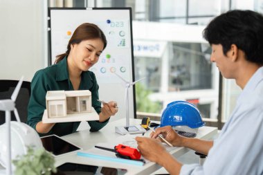 Bir kadın, modern ofis ortamında sürdürülebilirliği vurgulayan ESG stratejilerini bir meslektaşıyla tartışırken mimari modelini sunar.