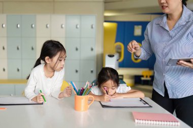 Bir öğretmen, genç öğrencilere yaratıcı faaliyetlerde bulunurken yardımcı olur, sınıfta olumlu bir öğrenme ortamı oluşturur..
