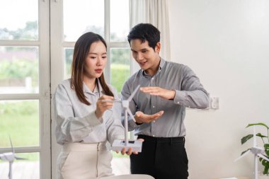 Bir erkek ve kadın coşkuyla bir rüzgar türbini modelini tartışıyor, ESG 'ye olan bağlılıklarını ve sürdürülebilir iş uygulamalarını ofis ortamında sergiliyorlar..