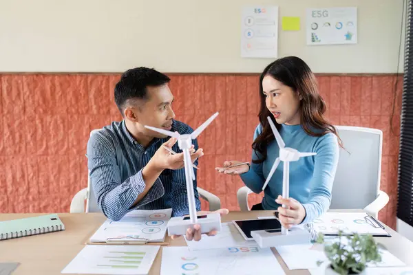 ESG stratejileri üzerinde işbirliği yapan, rüzgar türbini modellerini analiz eden ve yenilenebilir enerji girişimlerini tartışan iki profesyonel.
