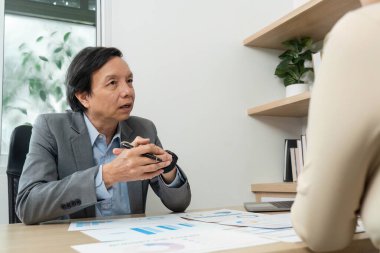 Bir iş adamı, modern ofis ortamında mali raporları analiz eden bir meslektaşıyla diyalog kurar..