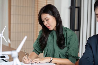 Profesyonel bir kadın sürdürülebilirlik toplantısı sırasında, ESG ilkelerine olan bağlılığını yansıtan notlar alır..