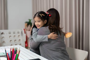 Genç bir kız annesiyle sıcak bir kucaklaşmayı paylaşır, rahat bir ev ortamında sevgi ve bağ gösterir..