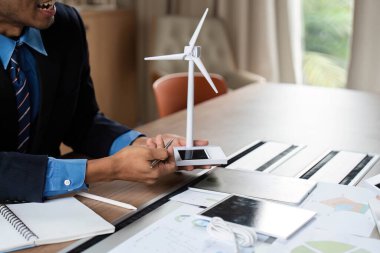 Bir iş adamı ESG toplantısında sürdürülebilir enerji çözümlerini vurgulayan bir rüzgar türbini modeli sundu.