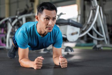Bir adam spor salonunda tahta egzersizi yapıyor. Vücut yapısının bir parçası olarak temel dayanıklılık ve denge üzerine odaklanıyor..