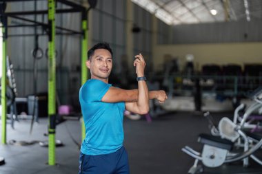 Formda bir adam spor salonunda kollarını açar, esnekliğe odaklanır ve yoğun bir antrenmana hazırlanır..