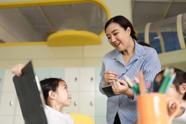 Bir öğretmen genç bir öğrenciyle iletişim kurar, öğrenme materyallerini tartışır ve parlak bir sınıf düzenine katılmaya teşvik eder..