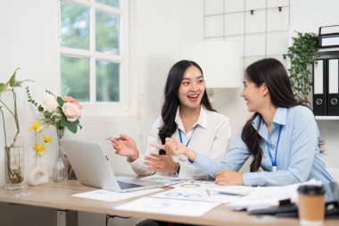 İki bayan meslektaşı, parlak bir ofis ortamında dizüstü bilgisayardaki proje belgelerini incelerken verimli bir sohbete girişiyor..
