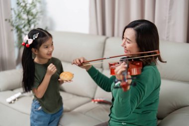Bir anne ve kızı, kız keman çalarken neşeli bir anı paylaşıyor. Aile ve müziğin neşesini vurguluyor..
