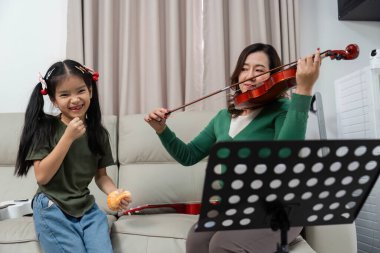 Bir anne ve kızı, keman çalarken neşeli bir anı paylaşıyor, müzik yoluyla aile bağlarını vurguluyorlar..