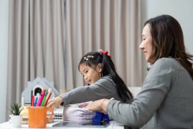 Genç bir kız, okul hazırlıklarının heyecanını vurgulamak için annesinin yardımıyla çantasını hazırlıyor..