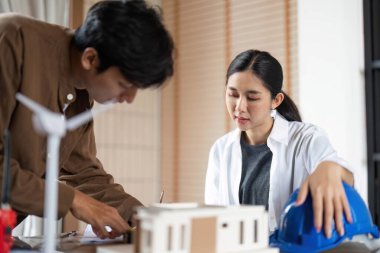 İki mimar çevre dostu inşaat planlarını tartışırken aynı zamanda modern bir çalışma alanının model ve planlarını gözden geçiriyorlar..