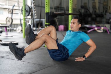 Spor salonunda bisiklet mekiği çeken atletik bir adam. Temel dayanıklılık ve spor rutinine odaklanıyor..