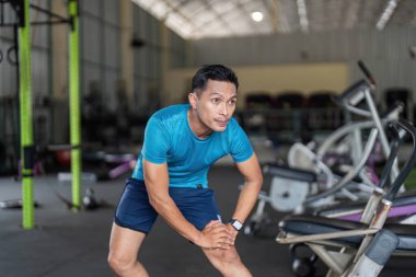 Formda bir adam spor salonunda esneme hareketleri yapar, performansı artırmak için esneklik ve ısınma egzersizlerine odaklanır..