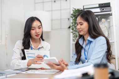 İki iş kadını, modern bir ofiste etkili iletişim ve işbirliğini vurgulayan dijital cihazlar kullanarak görüşlerini paylaşıyor..