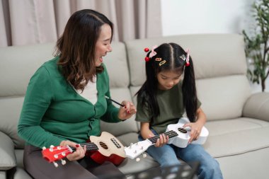 Bir anne ve kızı, müzik yolculuklarında eğlence ve yaratıcılığı vurgulayarak ukulele çalarken kahkahalarını paylaşıyor..