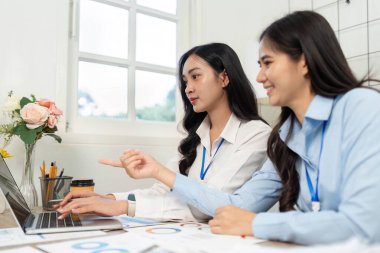 Bir dizüstü bilgisayara odaklanmış iki profesyonel fikir alışverişinde bulunuyor ve modern bir çalışma alanında takım çalışmasını teşvik ediyorlar..