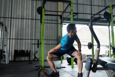 Erkek bir sporcu spor salonunda çömelir, güç gösterisi yapar ve spor salonunda formda ilerleme kaydeder..