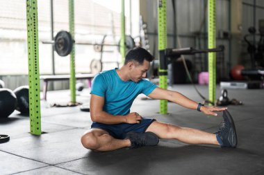 Odaklanmış bir adam spor salonunda bacağını uzatır, spor yaparken spor yapmaya ve esnekliğe olan bağlılığını gösterir..