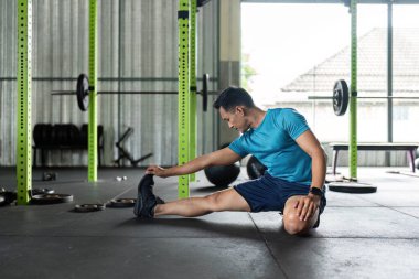 Bir adam spor salonunda bacağını esneterek esnekliğini arttırır ve antrenmanlara hazırlanır. Fitness ve sağlık konseptleri için mükemmel..