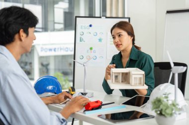 Bir kadın, modern bir çalışma alanında meslektaşıyla ESG girişimleri hakkında düşünceli bir konuşma yaparken mimari modelini açıklıyor..