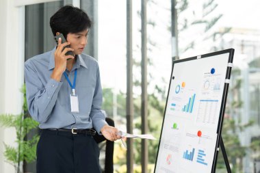 Bir işadamı, modern ofis ortamında çizelge ve grafikleri analiz ederek bir telefon görüşmesi yapar..